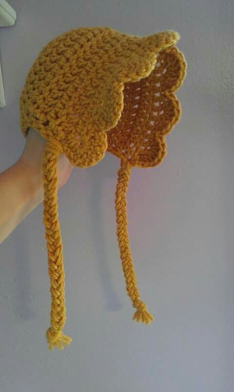 a crocheted hat hanging on the wall with someone's hand holding it