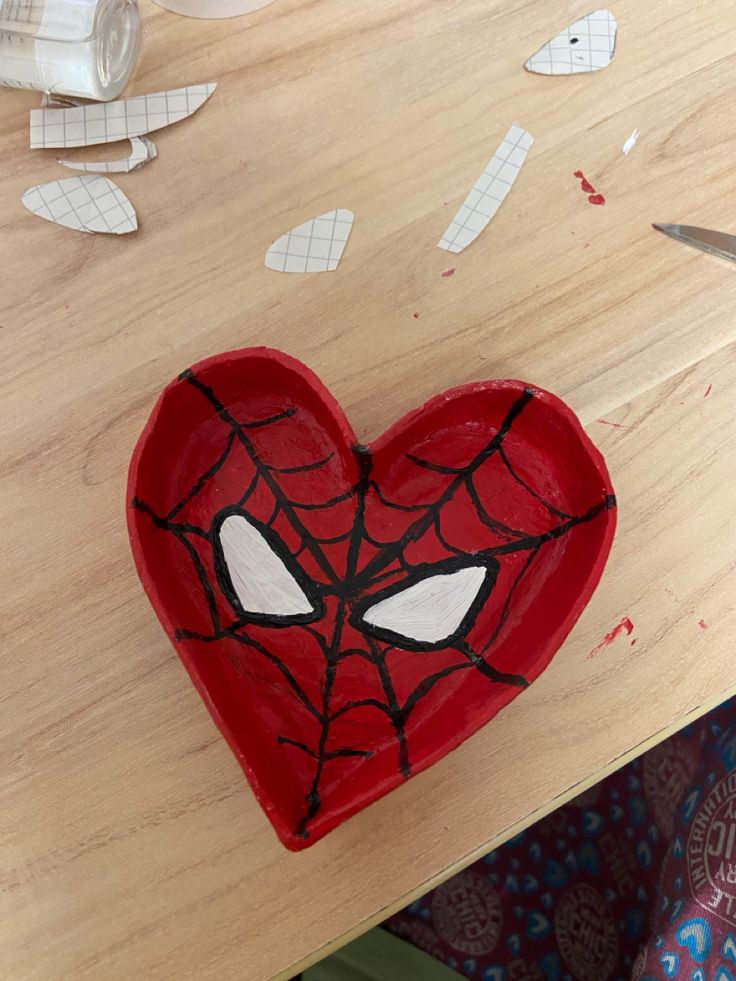 a heart shaped bowl with spiderman's face painted on it and cut out pieces of paper