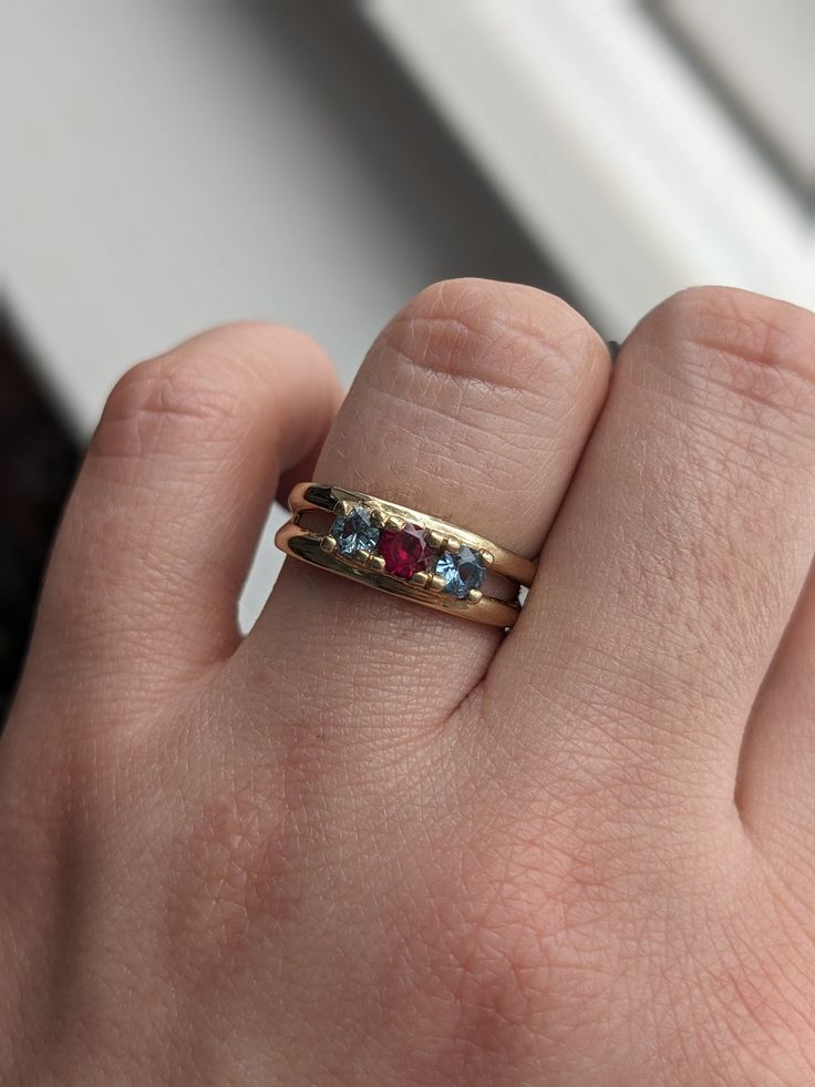 This beautiful ring features a bright pinkish red ruby flanked by two blue spinels. The stones are prong set and nested into a chunky split band. The band is cast in 14k yellow gold and has a nice feel and heft to it. The total weight is 4.14 grams. The size fits between a 6.5-6.75. This ring could be resized if needed by your local jeweler. The unusual color combination and the vibrancy of the stones make this piece extra special, the photos don't quite do it justice. Vintage Ruby Birthstone Ring, Vintage Ruby Birthstone Ring With Accent Stones, Vintage Style Ruby Birthstone Ring, Vintage Gold Ruby Ring With Three Stones, Vintage Yellow Gold Ruby Birthstone Ring, Stackable Wedding Rings, Chunky Wedding Rings, Chunky Wedding Band, Elegant Watches Women