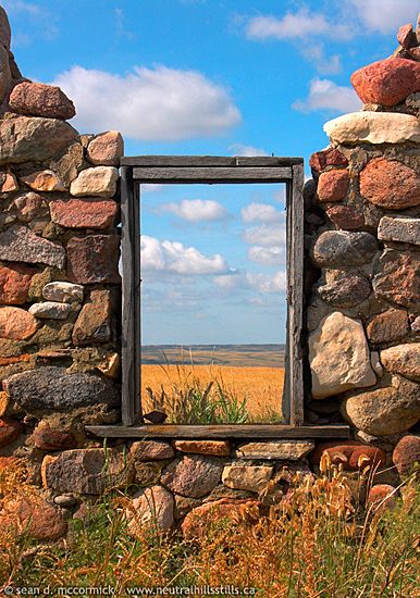 an old stone wall with a mirror in the middle and grass on the other side