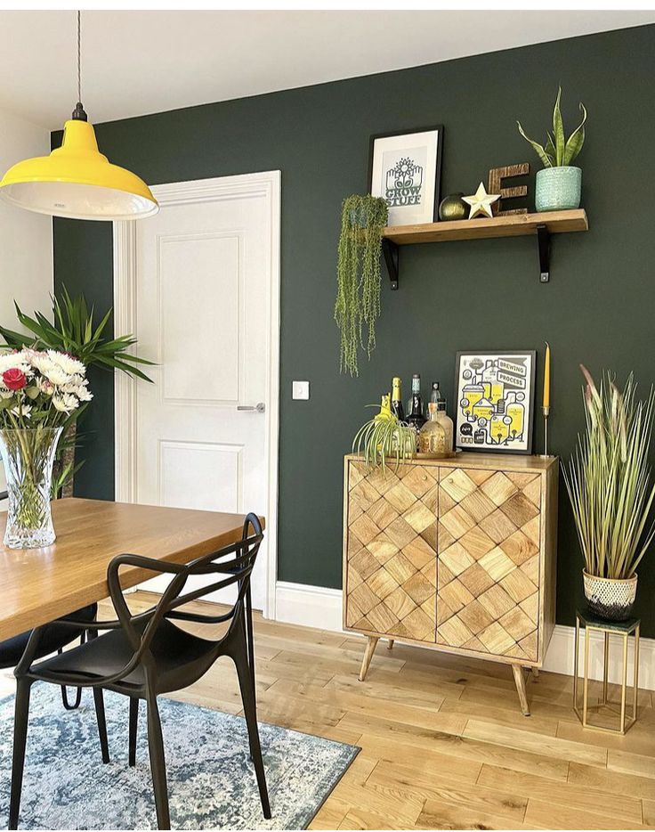 a dining room with green walls and wooden floors, plants on the shelf above the table