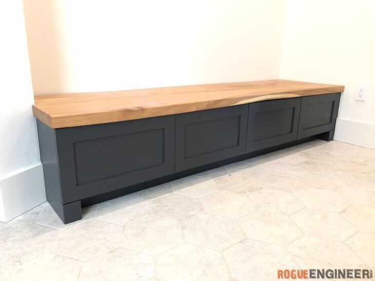 a large wooden bench sitting on top of a tile floor next to a white wall