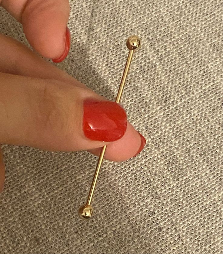 a woman's hand with red nail polish and gold bobby pin