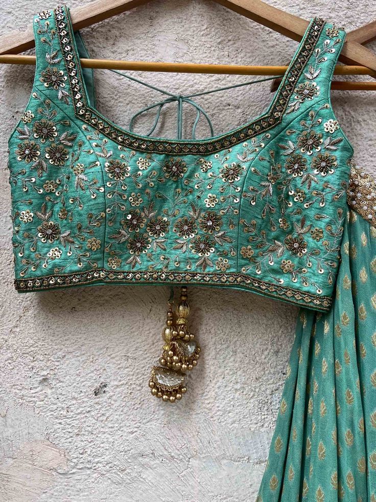 A three-piece jade green zari lehenga set from the Priti Sahni collection. This beautiful georgette small butti green lehenga with a heavy border of sequin, pearl and zari work detail with green accent is paired with a raw silk green blouse with sequin and zardosi embroidery detail all over. The lehenga has side hanging ball tassels to the waistline. And the blouse has a sequins tassel tie-up at the back. This outfit is completed with a sequin tulle dupatta with jade green accent in net material Green Embellished Pre-draped Saree For Wedding, Festive Green Anarkali Set With Unstitched Blouse, Green Anarkali Set With Unstitched Blouse For Festive Occasions, Green Lehenga With Unstitched Blouse In Chinon, Designer Embellished Green Lehenga, Green Bollywood Embellished Lehenga, Green Bollywood Lehenga Embellished, Green Bollywood Style Embellished Lehenga, Bollywood Style Green Embellished Lehenga