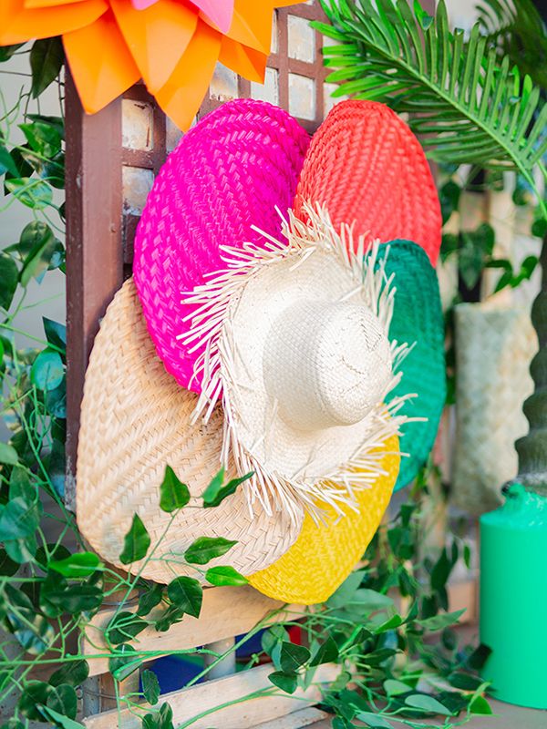 colorful straw hats are hanging from a wooden rack in front of green plants and greenery