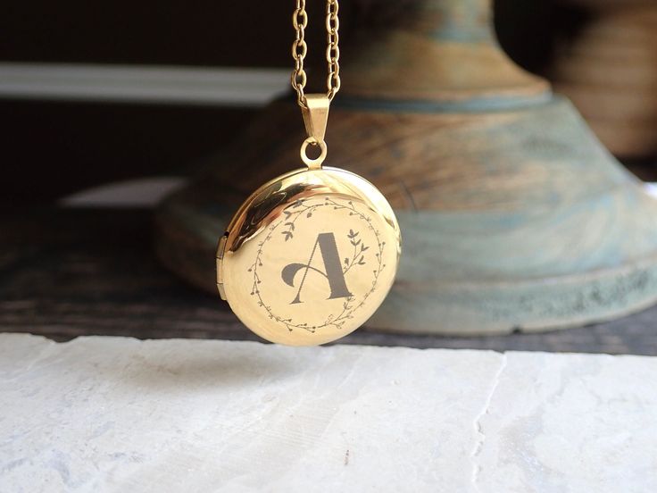 "Beautiful and classic, this round Victorian-inspired locket necklace features places for two photos inside. Personalize yours a vintage calligraphy initial with a floral motif surround. This treasured keepsake pendant and chain are both 14k gold plated stainless steel so are both hypo-allergenic and tarnish proof.   This locket isn't just a piece of jewelry; it's a vessel for your most precious memories. Whether it's a token of love, a symbol of a cherished bond, or a memento of a significant moment, this customizable gold locket holds the promise of preserving what matters most to you. Wear it close to your heart, carrying a photo, a tiny keepsake, or a secret message--whatever holds significance for you. Its versatile style seamlessly complements any outfit, making it a timeless additio Classic Personalized Round Pendant Locket Necklace, Classic Personalized Round Locket Necklace, Classic Round Locket Necklace As Gift, Gold Round Locket Necklace With Engraving Option, Classic Round Locket Necklace For Gift, Classic Personalized Locket Necklace For Wedding, Yellow Gold Round Locket Necklace For Mother's Day, Gold Round Locket Necklace For Mother's Day, Mother's Day Yellow Gold Round Locket Necklace