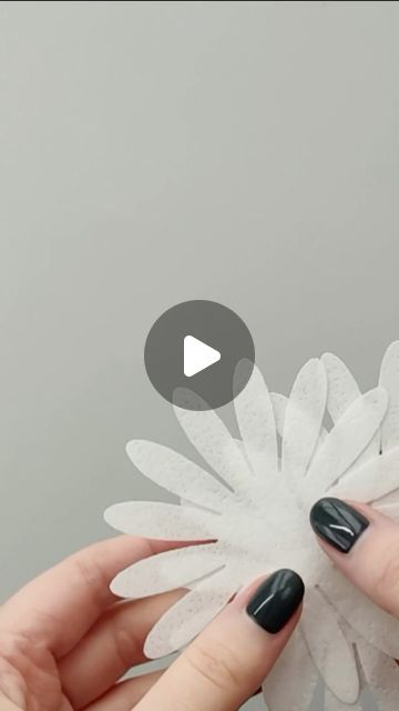 two hands are holding a white flower with black nail polish on it and one hand is holding an object