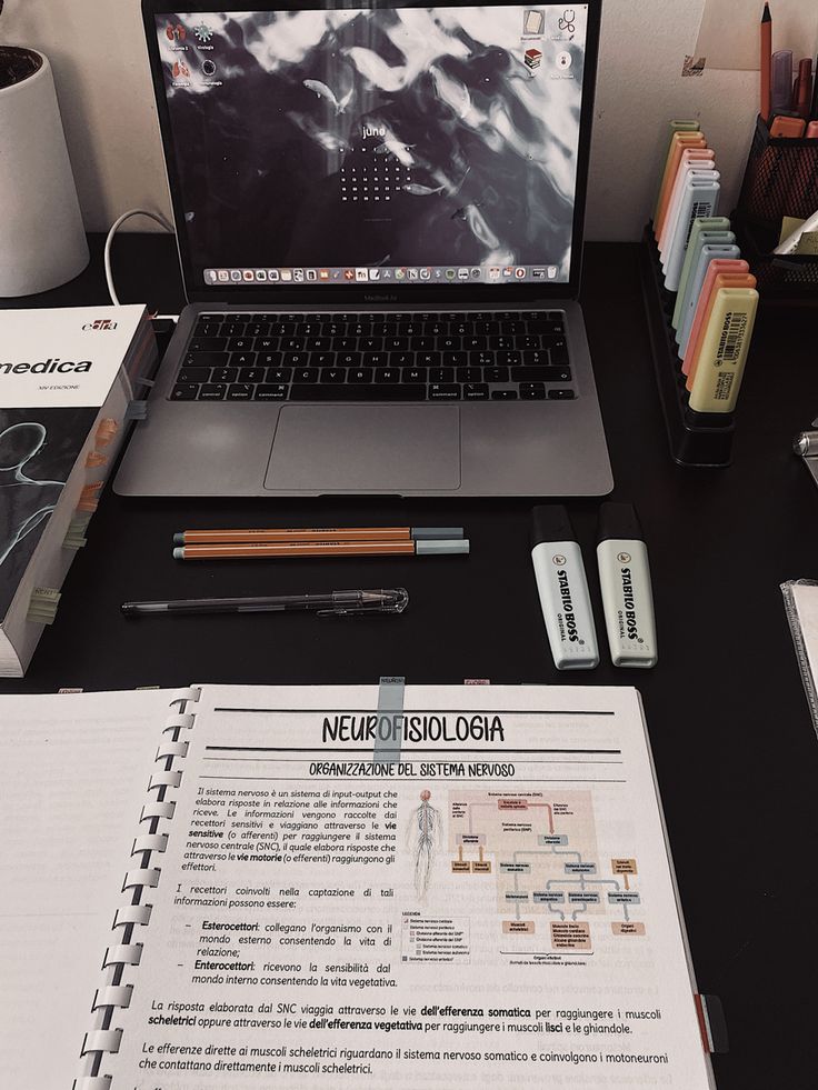 an open laptop computer sitting on top of a desk next to a pile of books