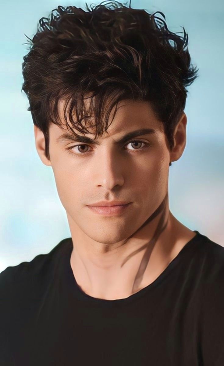 the young man is posing for a photo with his hair blowing in the wind and wearing a black t - shirt