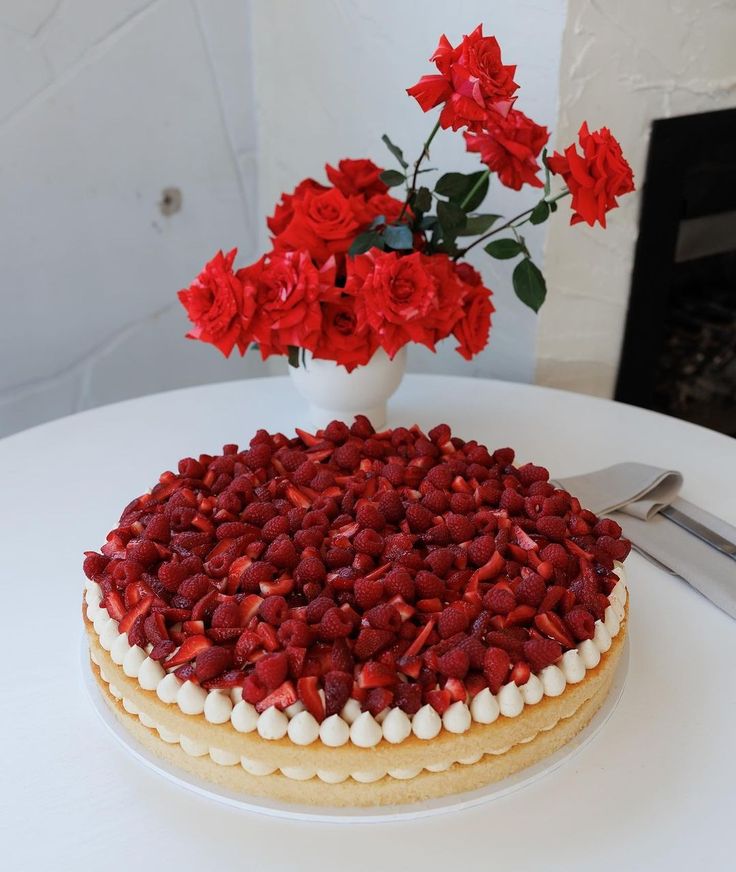 a cake on a table with red flowers in the vase and knife next to it