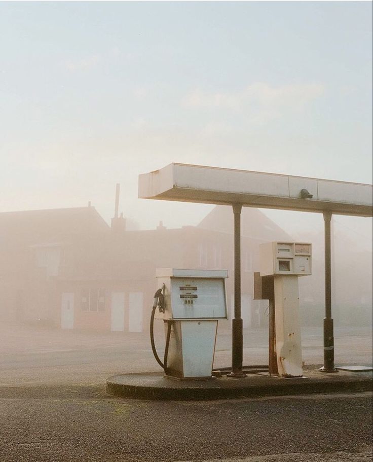 two old gas pumps sitting in the middle of a parking lot on a foggy day