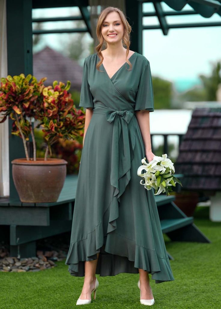 a woman in a green dress holding a bouquet and smiling at the camera while standing on grass