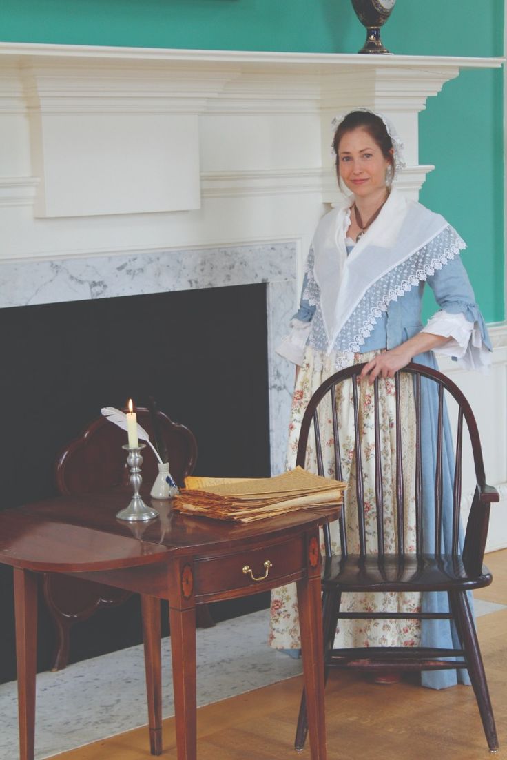 a woman standing next to a table with a candle on it in front of a fireplace