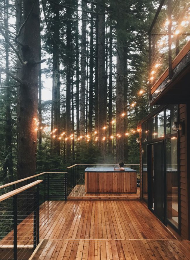 a wooden deck with hot tub surrounded by trees and string lights hanging from the ceiling