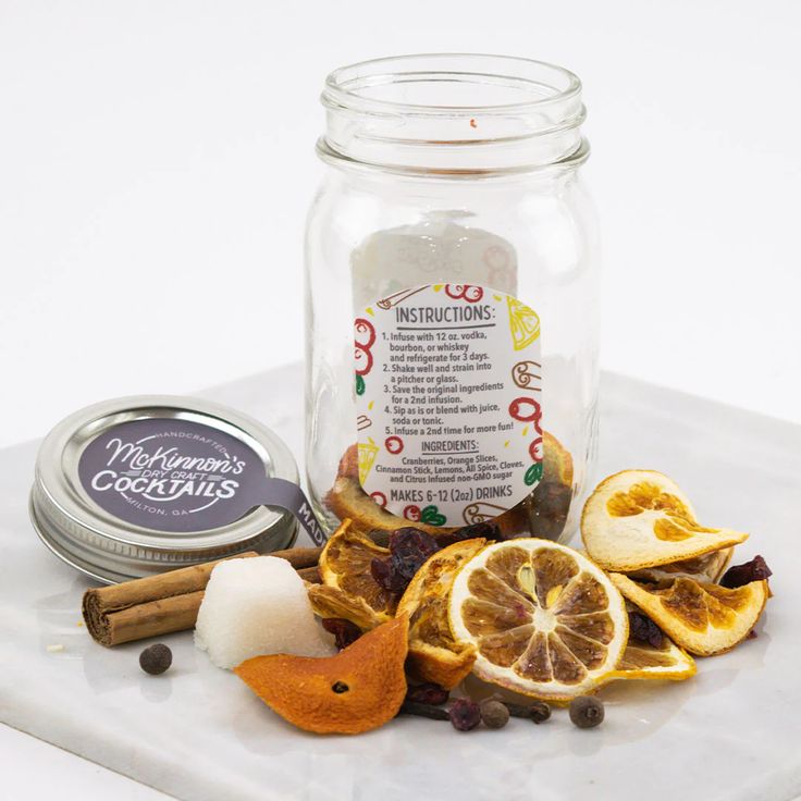 a jar filled with orange slices and cinnamons next to other ingredients on a white surface