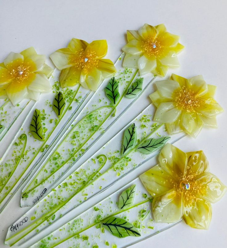 yellow flowers are arranged on white sticks with green leaves and dots in the middle, as well as water droplets