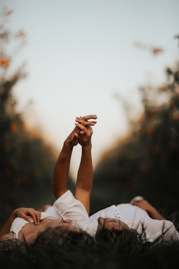 two people laying in the grass with their hands on each other's shoulders,