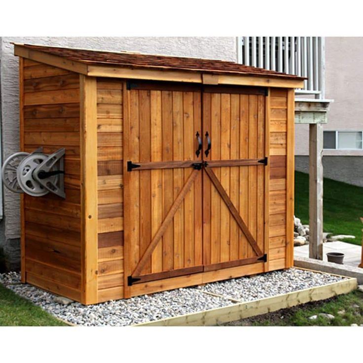 a wooden storage shed with sliding doors on the side and gravel in front of it