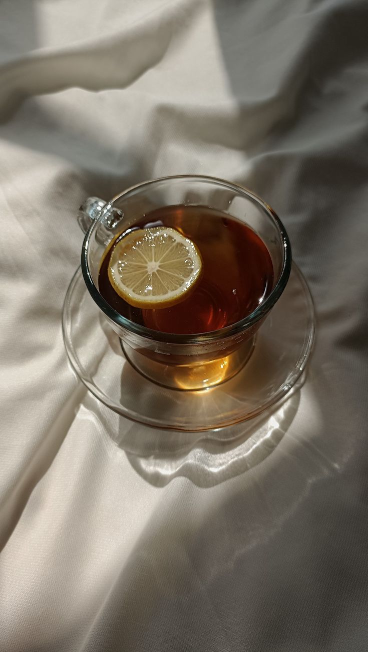 a glass cup filled with tea and a slice of lemon on top of white fabric