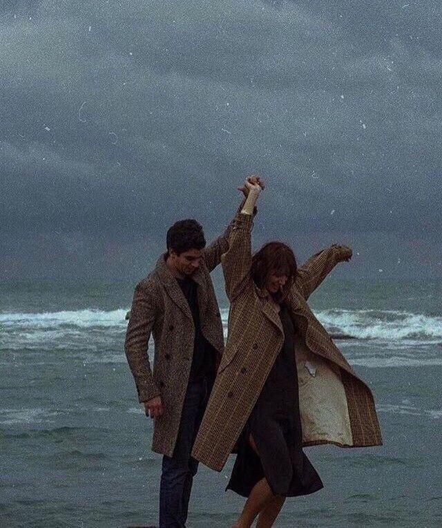 a man and woman standing on the beach with their arms in the air