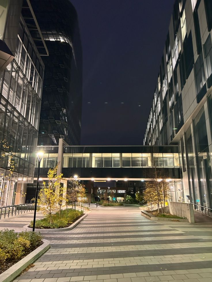 an empty city street at night with tall buildings in the back ground and lights on