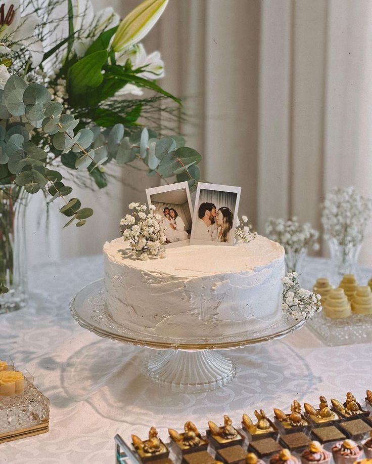 a table topped with a white cake covered in frosting and surrounded by desserts