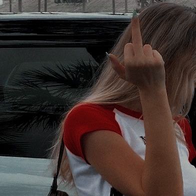 a woman standing in front of a car holding her hand up to the side while making a peace sign