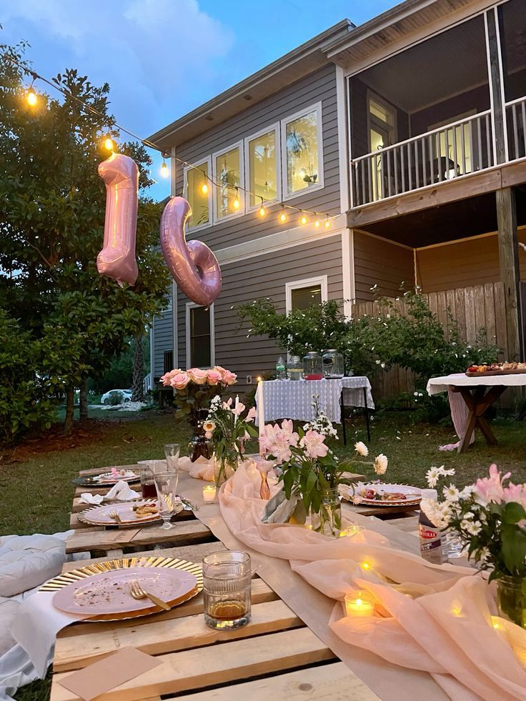 an outdoor table set up for a party with pink balloons and flowers on the table