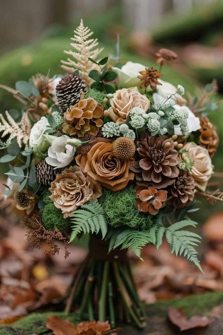 a bridal bouquet with pine cones and greenery on the ground in front of leaves