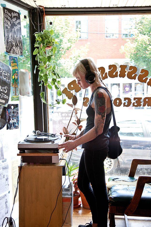 a woman with headphones is standing in front of a record player and looking into the window