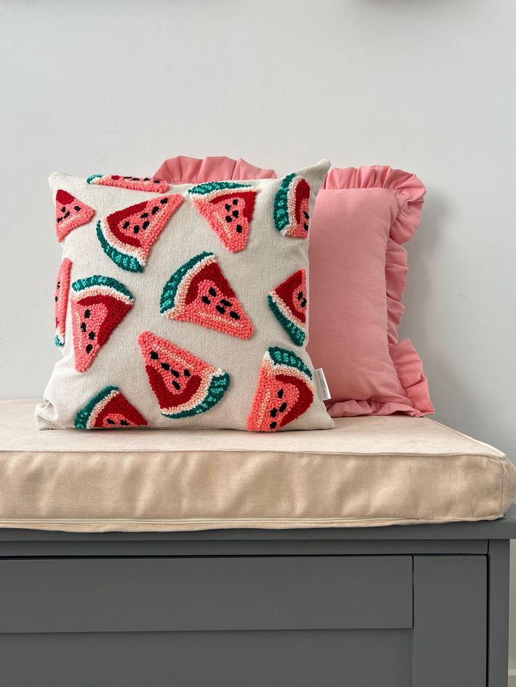 a watermelon pillow sitting on top of a bench next to a pink pillow