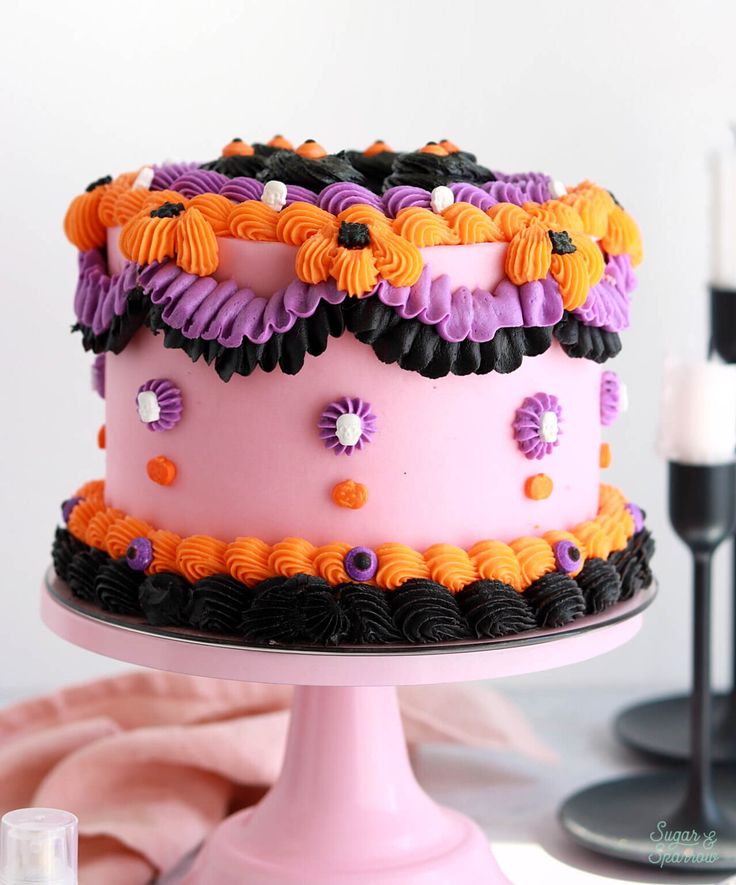 there is a pink cake with black and orange decorations on it