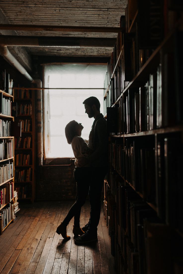 two people standing next to each other in front of a book shelf filled with books