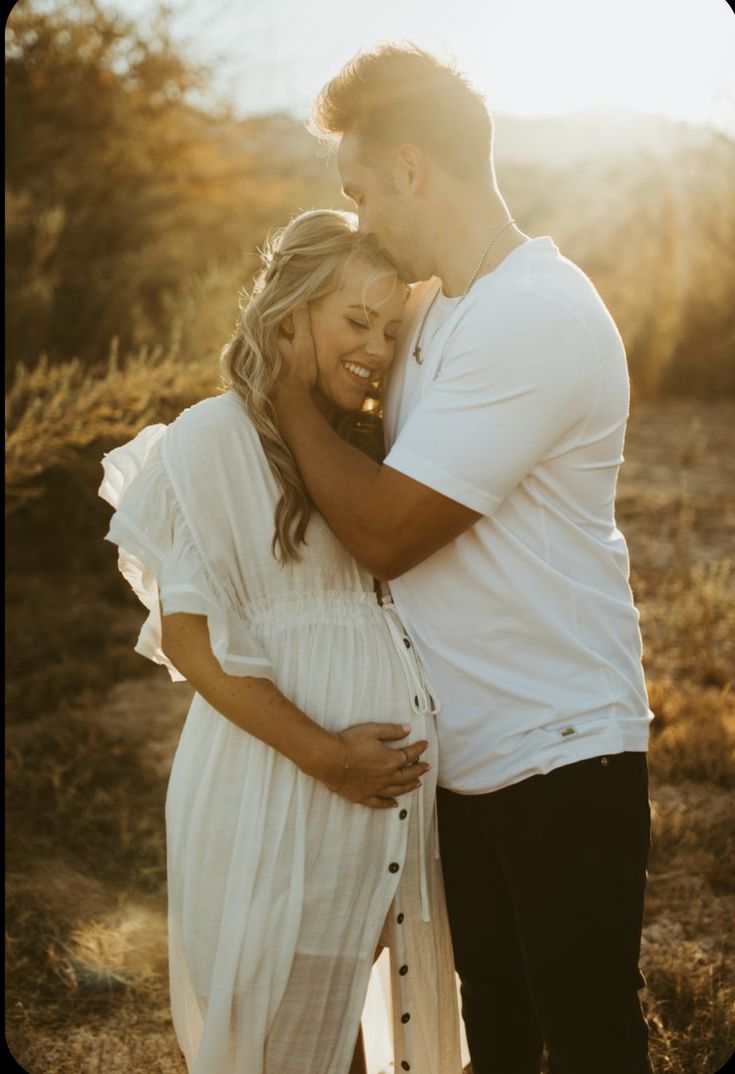 a man and woman embracing each other while standing in a field with the sun behind them