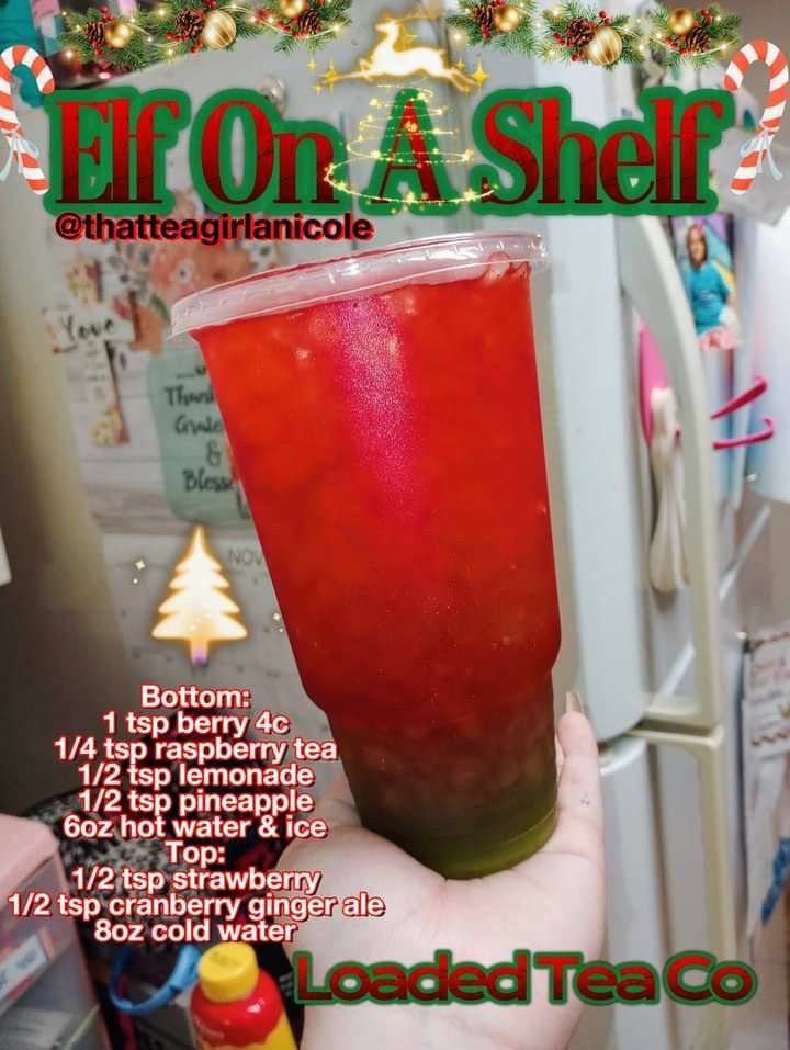 a person holding up a red drink in front of a refrigerator with christmas decorations on it