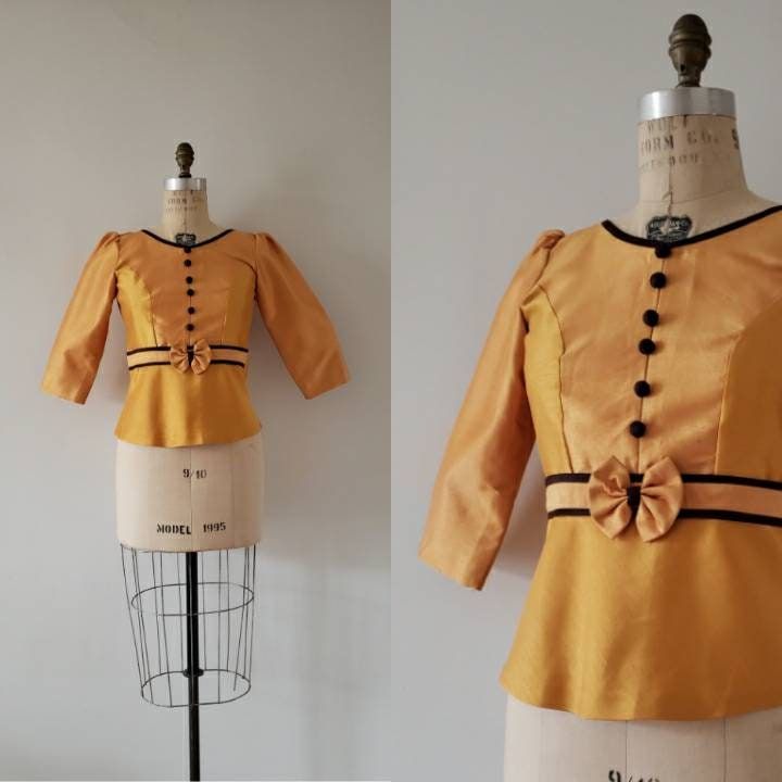 ABOUT 1960s mustard yellow silk structured blouse with chocolate brown trim at collar and waist. Blouse has 3/4 sleeves, chocolate brown buttons down front and a self-fabric bow. Blouse has self-fabric covered button closure at back. Made by: no tag. looks homemade Fabric: silk In good vintage condition. Has two faint stains at front near left of the bow ( please see picture) theres also writting on the inside of garment in a small spot (?) Would best fit approximate size extra small. Please refer to below measurements for proper fit. MEASUREMENTS Approximate FLAT measurements: Length: 22 inches Chest: 17 inches Waist: 15 inches For more Items like this one visit https://www.etsy.com/shop/pinkparadevintage Yellow Fitted Top For Office, Fitted Yellow Top For Office, Fitted Brown Blouse For Party, Vintage Brown Party Top, Fitted Gold Blouse For Office, Mustard Fitted Tops For Work, Fitted Vintage Gold Blouse, Fitted Mustard Top For Work, Vintage Gold Fitted Blouse