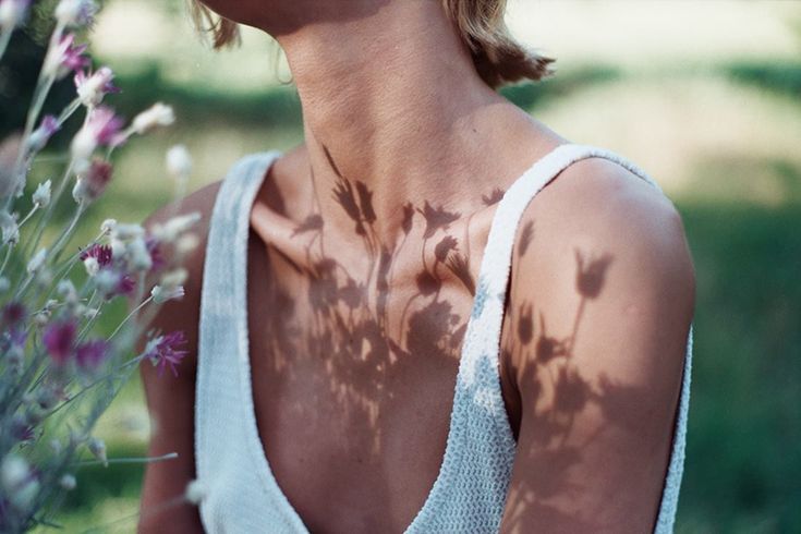 a woman standing in front of flowers with her back turned to the camera, wearing a white tank top