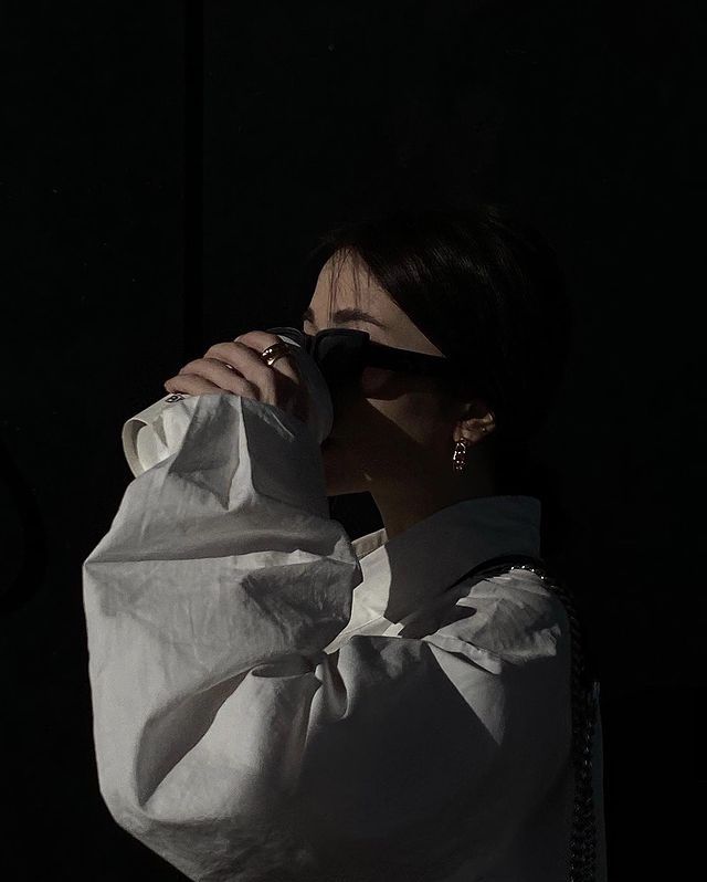 a woman in white shirt and sunglasses drinking from a cup with her hand over her face