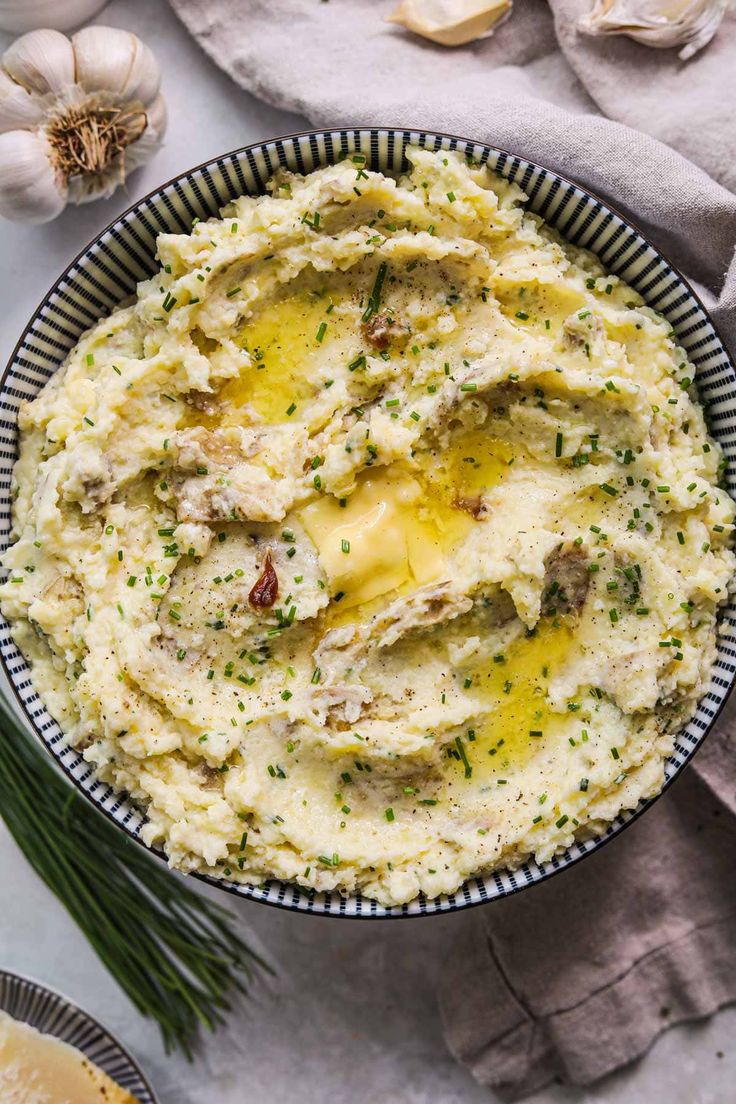 a bowl filled with mashed potatoes on top of a table next to garlic and herbs