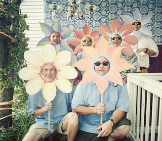 some people are sitting on the porch with paper flowers in front of them and one person is holding a large flower