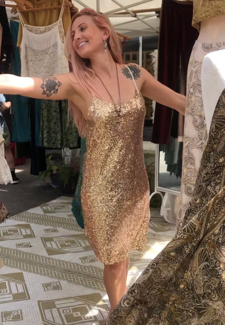 a woman in a gold sequin dress is smiling and pointing to the side with her right hand