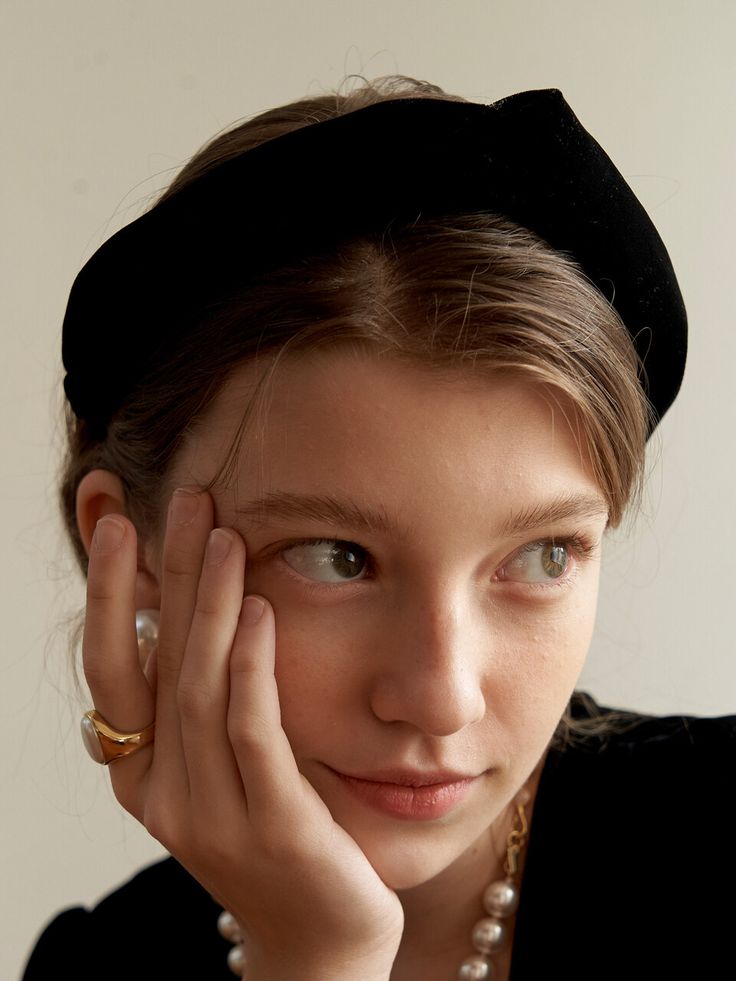 a young woman wearing a black hat and pearls is posing for the camera with her hands on her face