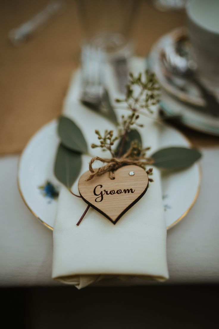 a wooden heart on a white plate with greenery in the shape of a flower