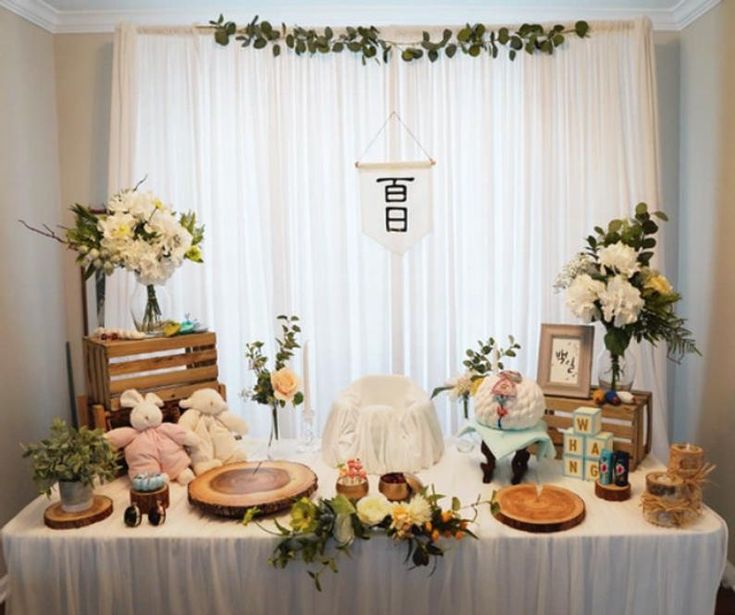 a table with flowers and stuffed animals on it in front of a white drapes