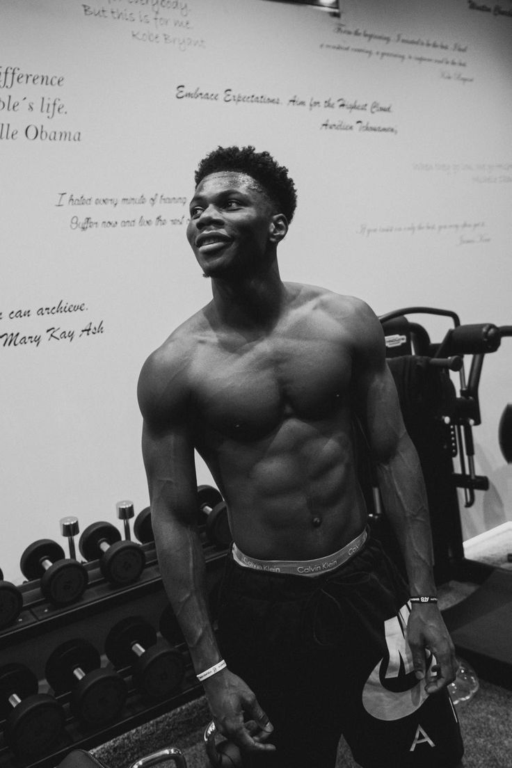 a shirtless man standing in front of a wall with dumbbells on it