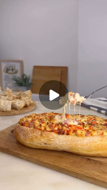 someone is drizzling cheese on top of a pizza in front of some bread