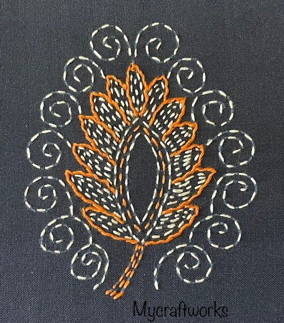 an orange and white embroidered design on a black cloth with circles around it, in the shape of a leaf