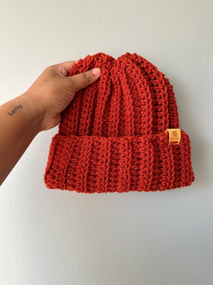 a hand holding up a red knitted beanie with a small wooden button on it