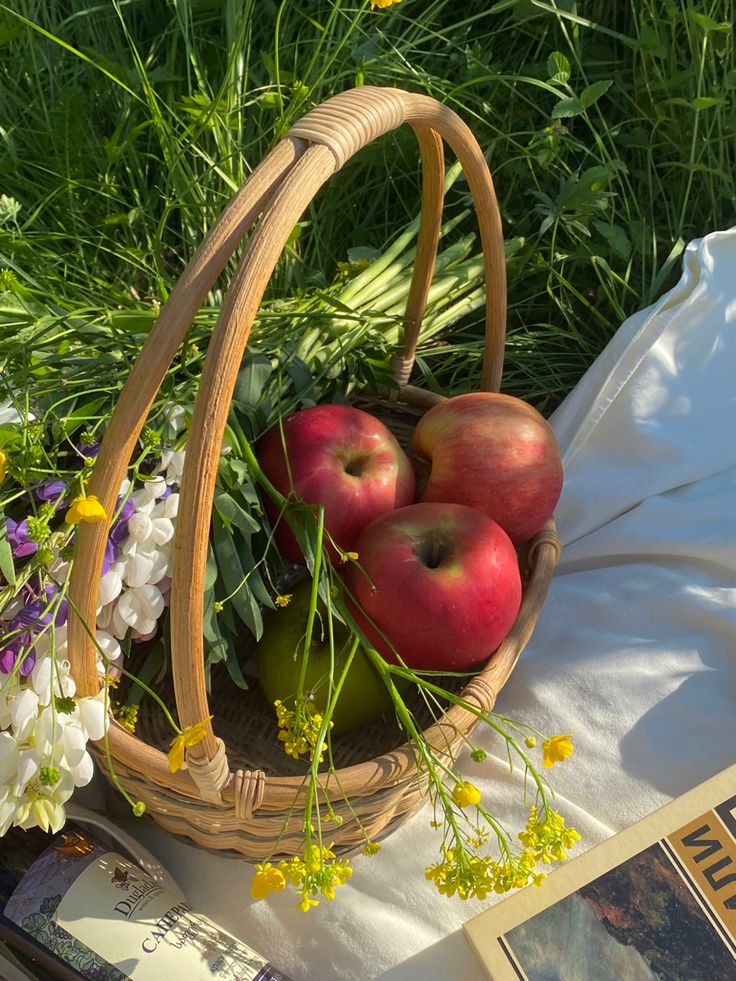 a basket filled with apples sitting on top of a table next to flowers and books