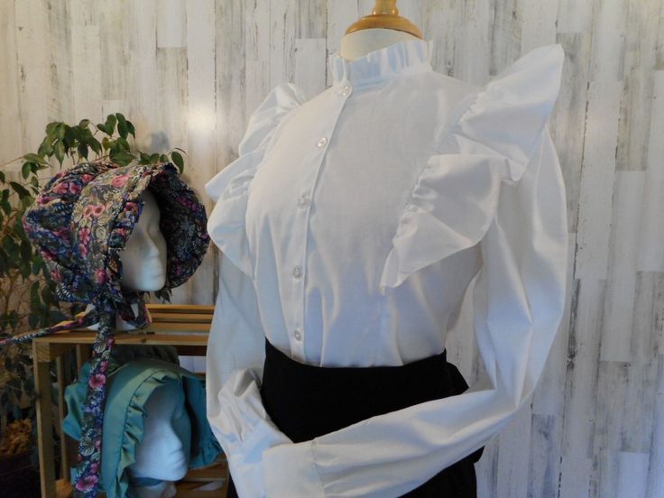 "Bonnets and Aprons sold separately. Amelia is a simple adaptation of the blouses worn on the prairie - very feminine and very modest. This front button blouse, slightly fitted, is accented with ruffles front and over the shoulder to the back. A double ruffle edges the neckline. Long sleeves are finished with a buttoned cuff. Available in misses sizes 8 to 20. FINISHED MEASUREMENTS AT BUSTLINE: Size 8: 35\" Size 10: 36\" Size 12: 37-1/2\" Size 14: 39-1/2\" Size 16: 41-1/2\" Size 18: 43-1/2\" Siz Spring Victorian Fitted Blouse, Fitted Ruffled Blouse For Daywear, Fitted Ruffle Blouse For Daywear, Victorian Ruffle Blouse For Daywear, Fitted Victorian Ruffle Top, Classic Fitted Ruffle Blouse, Classic Fitted Blouse With Ruffles, Victorian Fitted Ruffle Blouse, Victorian Fitted Ruffled Blouse